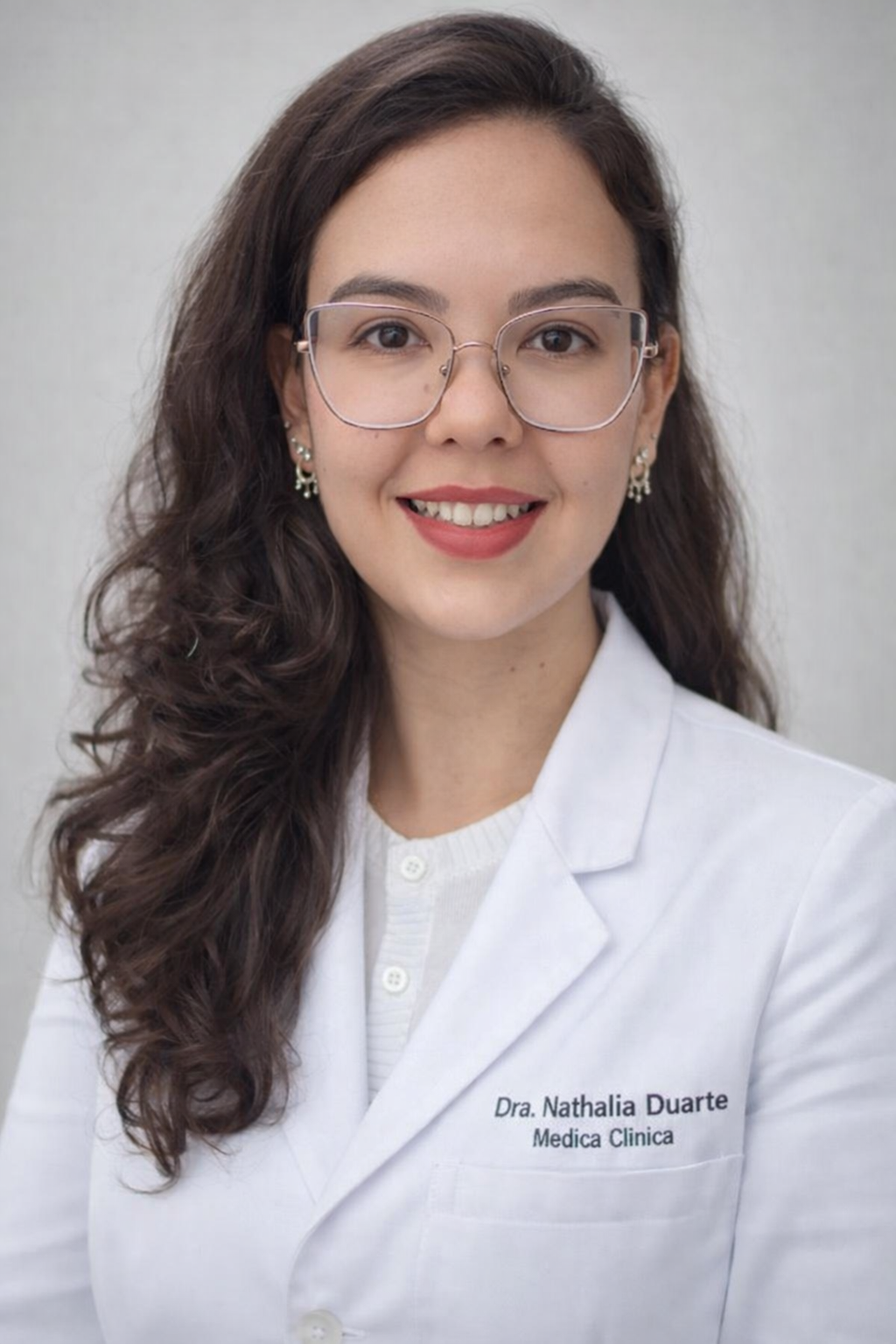 Dra. Nathalia Duarte, médica integrativa, sorrindo de jaleco branco